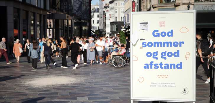 Passanten spazieren über den Strøget, die zentrale Einkaufsstraße von Kopenhagen. Davor ist ein ausgeblichenes Schild zu sehen, auf dem «God sommer og god afstand» (Guten Sommer und guten Abstand) geschrieben steht. Dänemark hebt die restlichen im Land geltenden Corona-Maßnahmen auf.