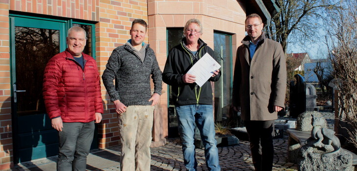 Wirtschaftsdezernent und Erster Kreisbeigeordneter Dr. Jens Mischak (rechts) übergibt gemeinsam mit Peter Sukdolak vom Amt für Wirtschaft und den ländlichen Raum (links), einen Förderbescheid über 75.000 Euro an den Steinmetz- und Steinbildhauerbetrieb von Johannes Voss und dessen Sohn Sebastian für die Anschaffung einer hochmodernen Brückensäge.