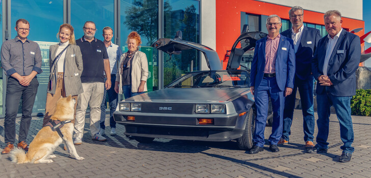Zurück in die Zukunft: Verantwortliche der fibit.business vor dem Kultauto der 1980er, dem DeLorean DMC-12
