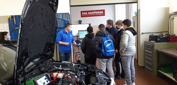 Kraftfahrzeugtechnikermeister Martin Schäfer (l.) zeigt einer Gruppe von Schülerinnen und Schülern der Gesamtschule Obersberg eine Fehlerdiagnose.